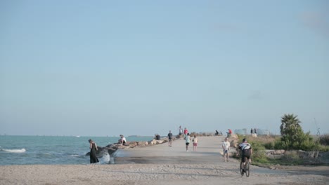 Gente-Y-Ciclista-Haciendo-Ejercicio-A-Lo-Largo-Del-Paseo-Marítimo-Al-Atardecer.