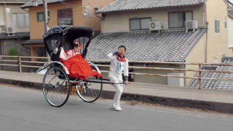 Rickshaw-pulled-by-running-man-carrying-women-down-road-in-Nara,-Japan