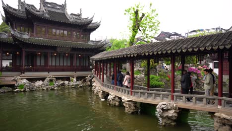 Visitors-walking-under-a-corridor-next-to-a-pond-in-the-Yuyuan-Garden,-Shanghai