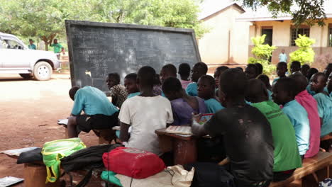 Outdoor-classroom-in-Kampala,-Uganda-with-children-learning-under-a-tree-on-a-sunny-day