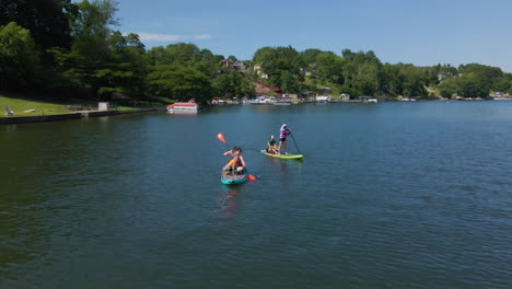 Women-Ride-Paddle-Boards-with-Child-and-Dog-on-Pennsylvania,-USA,-Lake-in-Summer