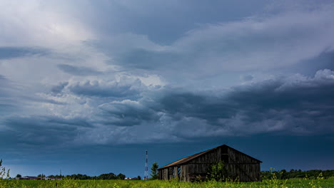 Storm-clouds-gather-over-an-old-barn-in-a-rural-field,-showcasing-nature's-power,-timelapse