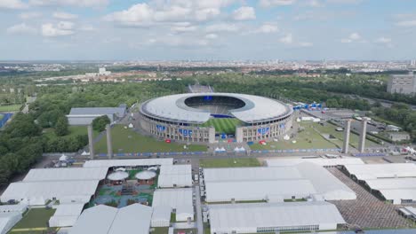 Toma-Aérea-Del-Estadio-Olímpico-Euro-2024-Viajando-A-La-Entrada-Campo-De-Fútbol-Estadio-Vacío-Y-Asientos-Clima-Soleado