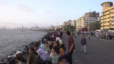 Tourists-at-Marine-Drive-beach-in-the-evening,-Mumbai-skyline-buildings-in-background