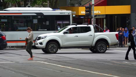 Busy-traffic-at-the-corner-of-Lonsdale-and-Swanston-streets-in-the-heart-of-Melbourne-bustling's-central-business-district-with-pedestrians-crossing-and,-cars-and-buses-driving-along-the-street