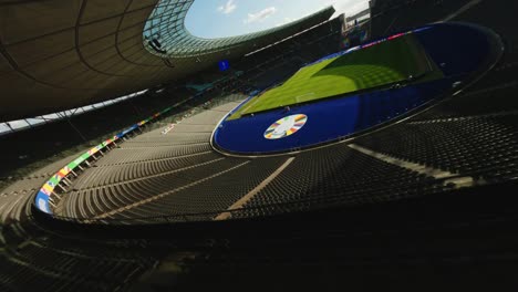 UEFA-EURO-2024-Olympic-Stadium-Berlin-FPV-drone-flying-over-empty-seats-towards-green-football-pitch-over-UEFA-Logo-on-sunny-day