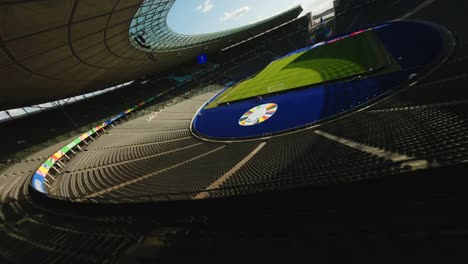 UEFA-Euro-2024-Olympiastadion-Berlin-FPV-Drohne-Fliegt-An-Einem-Sonnigen-Tag-über-Leere-Sitze-In-Richtung-Grünes-Fußballfeld-über-Dem-UEFA-Logo