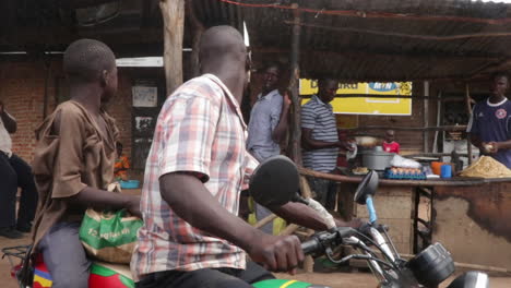 couple-of-brother-driving-in-Africa-remote-village-on-a-old-motorcycle-without-helmets,-giving-directions