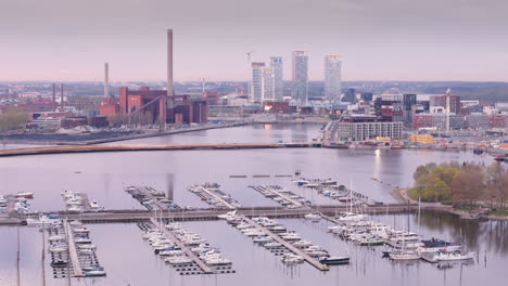 Drone-over-docked-boats-in-marina-and-view-toward-developed-waterfront,-Helsinki