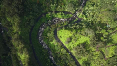 Luftaufnahme-Aus-Der-Vogelperspektive-Einer-Kurvenreichen-Straße-Durch-Einen-Leuchtend-Grünen-Berghang-Mit-Einem-Fluss,-Der-Durch-Ein-Kleines-Tal-Fließt