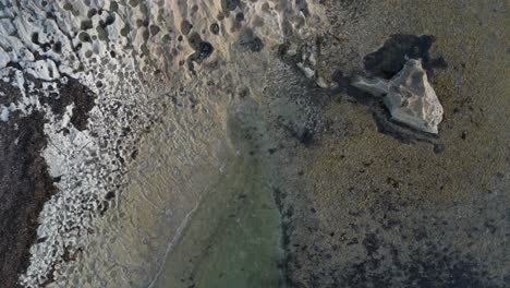 Aerial-top-down-shot-of-clear-water-of-ocean-reaching-rocky-shore-of-Cactus-Beach,-Australia