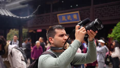 Hombre-Filmando-Con-Una-Cámara-Profesional-En-El-Templo-De-La-Ciudad-De-Dios-Rodeado-De-Chinos-Locales,-Shanghai