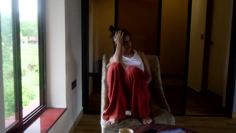 Woman-sitting-in-cozy-chair,-looking-out-the-window,-morning-light-streaming-in