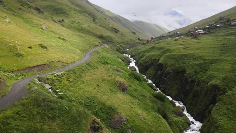 Eine-Malerische-Bergstraße-Schlängelt-Sich-Durch-üppige-Grüne-Täler,-An-Denen-Ein-Bach-Entlang-Fließt