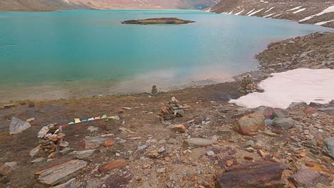 4K-fly-forward-drone-shot-revealing-prayer-flags,-cairns-,-Himalayan-Glacial-lake-with-island-in-the-middle-and-hanging-glaciers