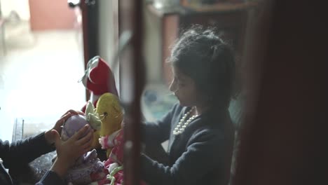 A-small-child-is-focused-on-playing-with-various-toys,-seated-indoors,-face-being-reflected-on-cabinet-window