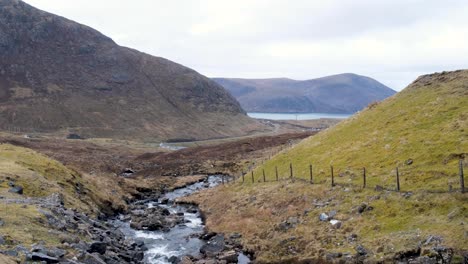 Scenic-landscape-view-overlooking-rugged-mountainous-terrain-and-free-flowing-stream-of-water-to-loch-lake-in-the-Outer-Hebrides-of-Scotland-UK