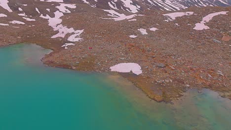 4K-pullback-drone-shot-revealing-hikers-sitting-on-the-banks-of-a-Himalayan-Glacial-lake-surrounded-by-snow-capped-mountains