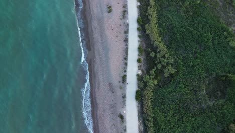 Zenithal-view-of-a-beach-with-waves-hitting-the-shore-at-sunset,-as-people-walk-and-exercise-along-the-shoreline