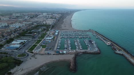 Pull-back-shoot-of-a-seaside-marina-at-sunset,-with-the-city-skyline-and-mountains