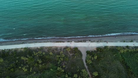 Aerial-view-with-inclination-of-a-beach-with-waves-hitting-the-shore-at-sunset,-as-people-walk-and-exercise-along-the-shoreline