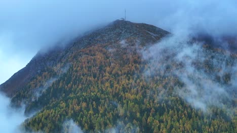 Saastal-Saas-Fee-Switzerland-aerial-drone-mountain-larch-forest-peak-moody-clouds-layer-gray-grey-rainy-fog-mist-Swiss-Alps-mountain-peaks-glacier-valley-pole-weather-station-to-the-right-motion