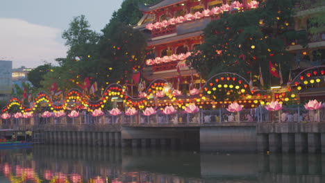 Farbenfroher-Buddhistischer-Tempel-Mit-Chinesischer-Vietnamesischer-Flagge-über-Dem-Flusswasser,-Nachts-Beleuchtet-Während-Der-Jährlichen-Buddhistischen-Vesak-Festlichkeiten-In-Südostasien