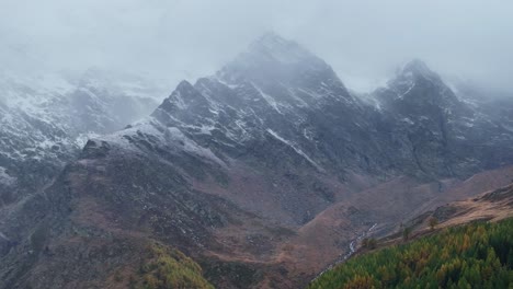 Fall-autumn-Saastal-Saas-Fee-Switzerland-aerial-drone-mountain-peaks-first-snow-dusting-cloud-layer-gray-grey-rainy-fog-mist-Swiss-Alps-mountain-peaks-glacier-valley-forward-pan-reveal