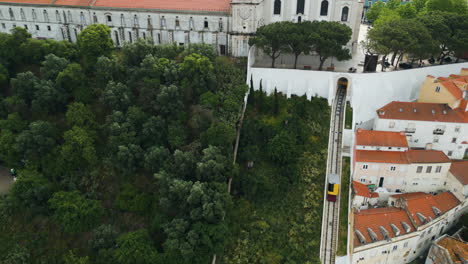 Aerial-view-following-a-yellow-funicular-lift-moving-uphill-in-cloudy-Lisbon