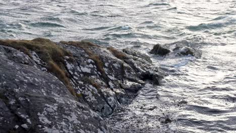 Scenic-close-up-view-of-ocean-waves-gently-lapping-against-rugged-rocky-outcrop-with-moss-in-the-wilderness-of-the-Outer-Hebrides-in-Scotland-UK