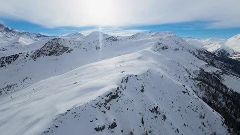 Vista-Aérea-De-Un-Vasto-Paisaje-Montañoso-Cubierto-De-Nieve-Con-Un-Cielo-Azul-Claro-Y-Luz-Solar-Brillante