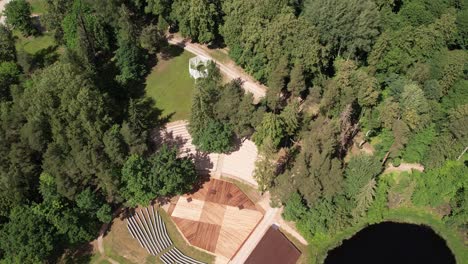 Vista-Aérea-Del-Escenario-De-Diklu-En-La-Aldea-De-Dikli,-Que-Muestra-El-Lugar-De-Actuación-Al-Aire-Libre-Rodeado-De-Exuberante-Vegetación-Y-Edificios-Cercanos.