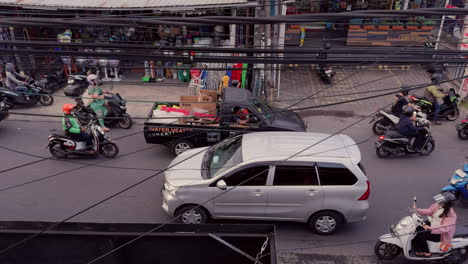 Una-Concurrida-Calle-De-Bali-Con-Coches,-Motos-Y-Líneas-Eléctricas-Aéreas-Cruzan-La-Escena.