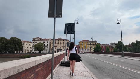 Walking-over-the-red-bricked-bridge-in-Verona,-Italy-with-the-view-over-river-Adige-and-panorama-of-the-city