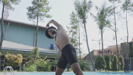 Vista-En-ángulo-Bajo-De-Un-Joven-Asiático-Levanta-Los-Brazos-Haciendo-Calentamiento-Antes-De-Nadar-En-La-Piscina