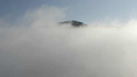 Drone-coming-up-through-clouds-to-reveal-mountain-summit