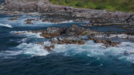 Flying-over-waves-breaking-on-rocky-cliff-off-north-coast-of-Maui,-Hawaii