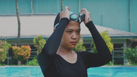 Nadadora-Asiática-Profesional-Con-Traje-De-Baño-Negro,-Gorra-De-Agua-Y-Gafas-Antes-De-Nadar-En-La-Piscina