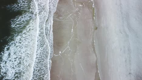 Beach-drone-shot-above-the-water-with-waves-breaking-on-the-shore