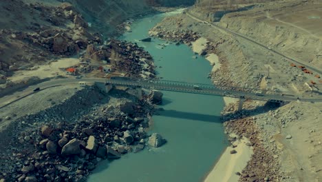 High-angle-view-of-a-bridge-joining-both-lands-with-vehicles-passing-over-it-in-Skardu,-Pakistan