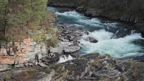 A-wild-river-rushes-through-a-deep,-narrow,-rocky-canyon-with-moss-covered-cliffs