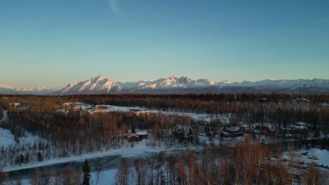 Paisaje-De-Alaska-Durante-La-Puesta-De-Sol-Con-Cabañas-En-Primer-Plano-Y-Montañas-En-Segundo-Plano.