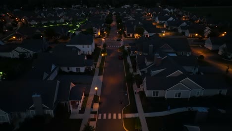 Vista-Aérea-Nocturna-De-Un-Tranquilo-Barrio-Suburbano,-Iluminado-Por-Farolas-Y-Luces-De-Casas,-Mostrando-Calles-Ordenadas-Y-Casas-Bien-Cuidadas