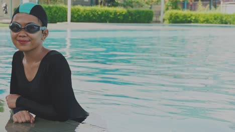 Una-Joven-Asiática-Usa-Gorro-De-Baño-Y-Gafas,-Parada-En-La-Piscina-Y-Mirando-A-La-Cámara.