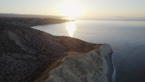 Eine-Atemberaubende-Luftaufnahme-Der-Küstenklippen-Zyperns,-Die-Bei-Sonnenaufgang-In-Goldenes-Sonnenlicht-Getaucht-Sind
