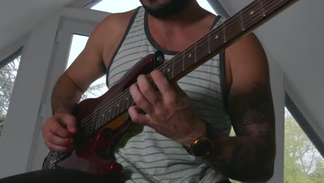 Man-playing-beautiful-red-electric-guitar-in-home-recording-studio