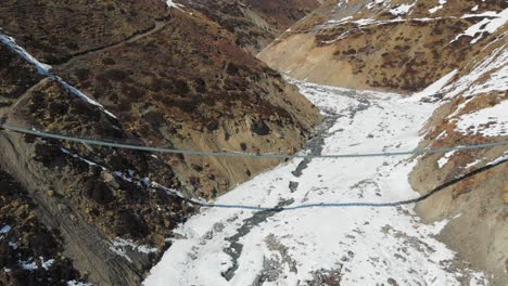 A-solo-trekker-walking-on-a-suspension-bridge-with-frozen-river-bed-below