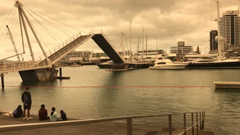 The-overcast-sky-casts-an-orange-hue-over-the-bascule-bridge-as-it-opens-upwards-as-a-few-tourists-look-on