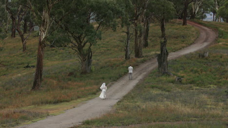 Una-Novia-Con-Su-Vestido-Blanco-Y-Velo-Camina-Hacia-El-Novio-Que-Está-De-Espaldas-Esperándola-En-Medio-De-Una-Carretera