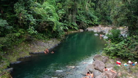 Gente-Relajándose-En-La-Orilla-Del-Río-De-La-Selva-Tropical-Del-Sendero-Angelito,-Antena-Delantera